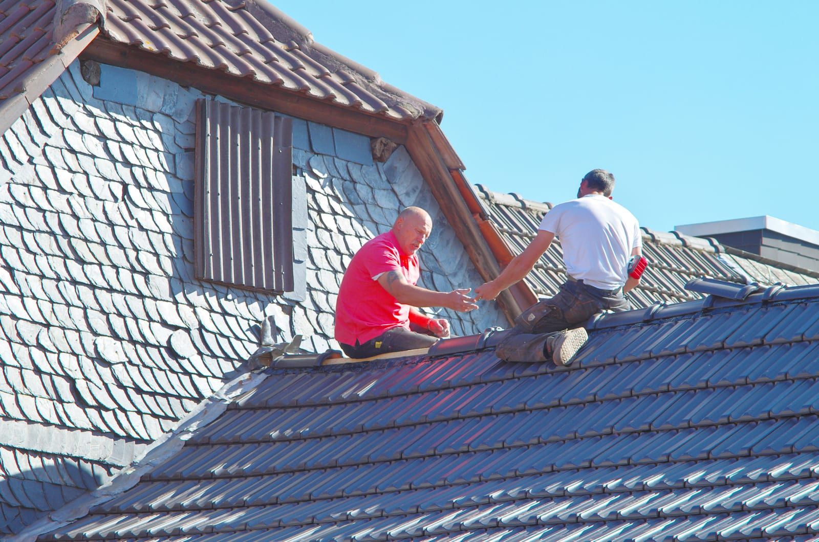 Deux couvreurs au travail sur une toiture en tuile, ardoise posée en pignon